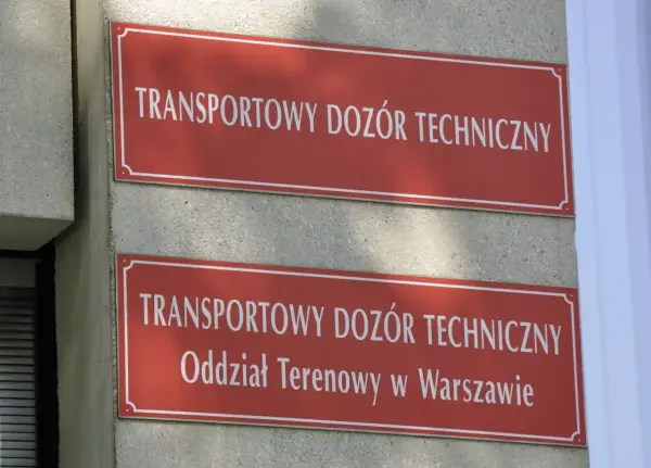 Dwa czerwone szyldy z białym napisem "TRANSPORTOWY DOZÓR TECHNICZNY". Dolny szyld zawiera dodatkowo "Oddział Terenowy w Warszawie". Miejsce, gdzie można uzyskać homologację.
