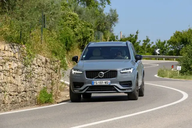 Szary Volvo XC90 2020 pokonuje zakręt na malowniczej, górskiej drodze.