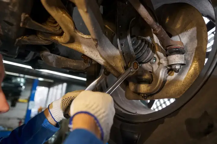 Mechanik dokręca śrubę w zawieszeniu samochodu kluczem.
