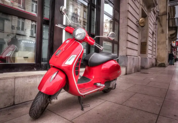 Czerwona Vespa na chodniku. Czy można nią jeździć mając prawo jazdy AM od ilu lat?