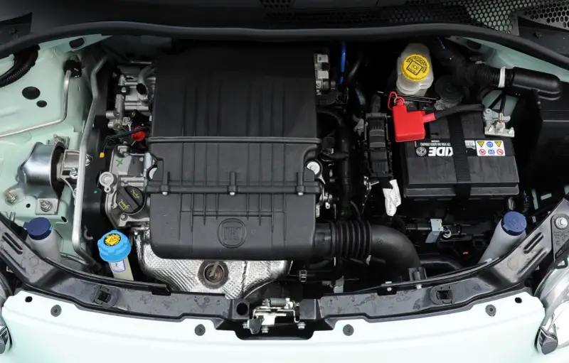 Silnik Fiata 500 L z widocznym logo FIAT na czarnej obudowie. Widać akumulator, płyny i elementy układu chłodzenia.
